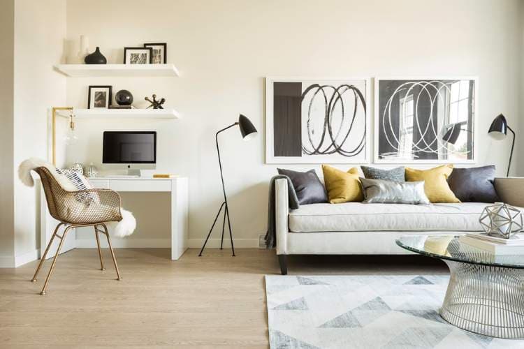Allwood Place – Living room corner with a home office nook featuring a desktop computer, and a daybed sofa with graphic throw pillows beneath framed abstract art.