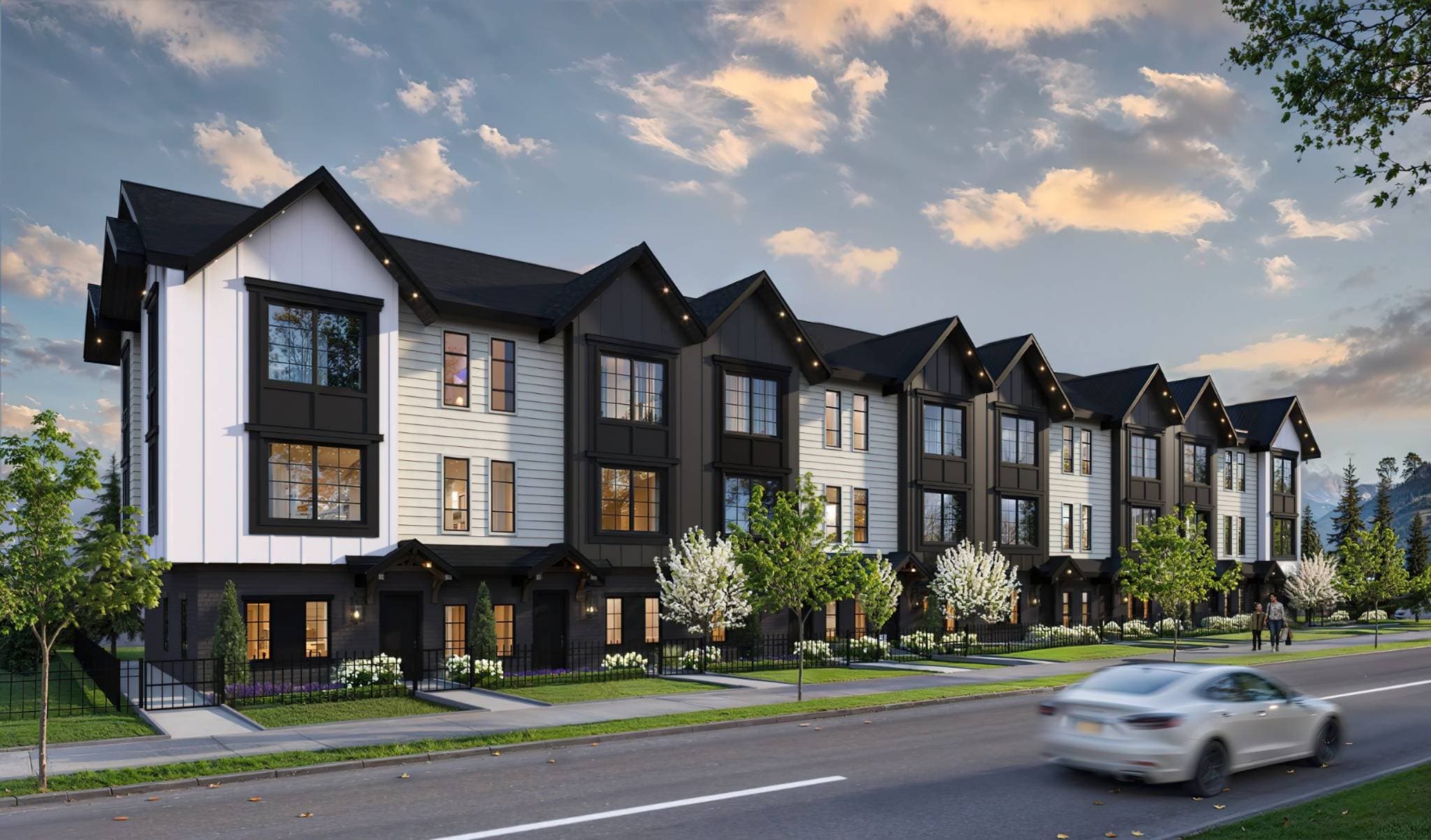 Bromley Brookswood – Dusk street-level rendering of a row of black-and-white gabled townhomes with individual front entries, landscaping, and a car driving past on the street.
