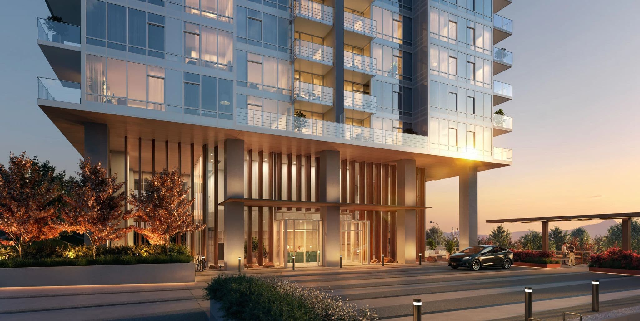 Ironwood – The building's street-level entrance at dusk, with a wood-slat canopy, glass doors, landscaping, and a car parked at the drop-off.