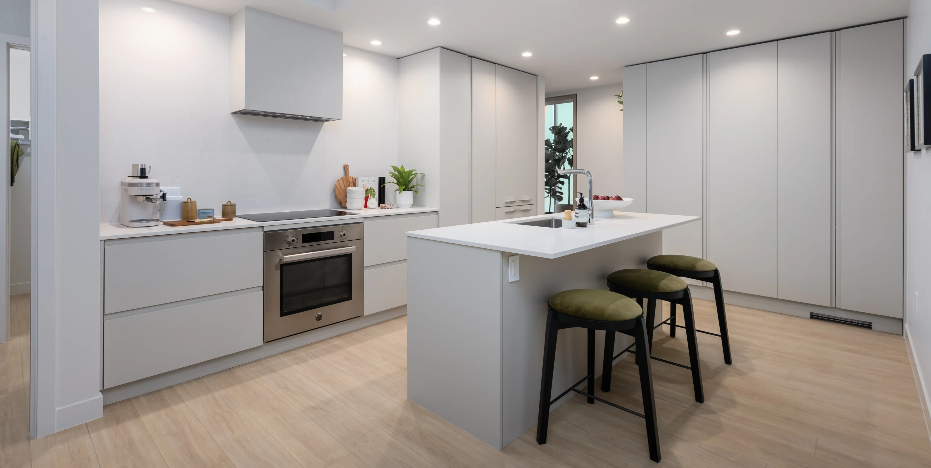 Ironwood – A white kitchen with a large island, black stools, built-in oven, induction cooktop, and floor-to-ceiling cabinetry.