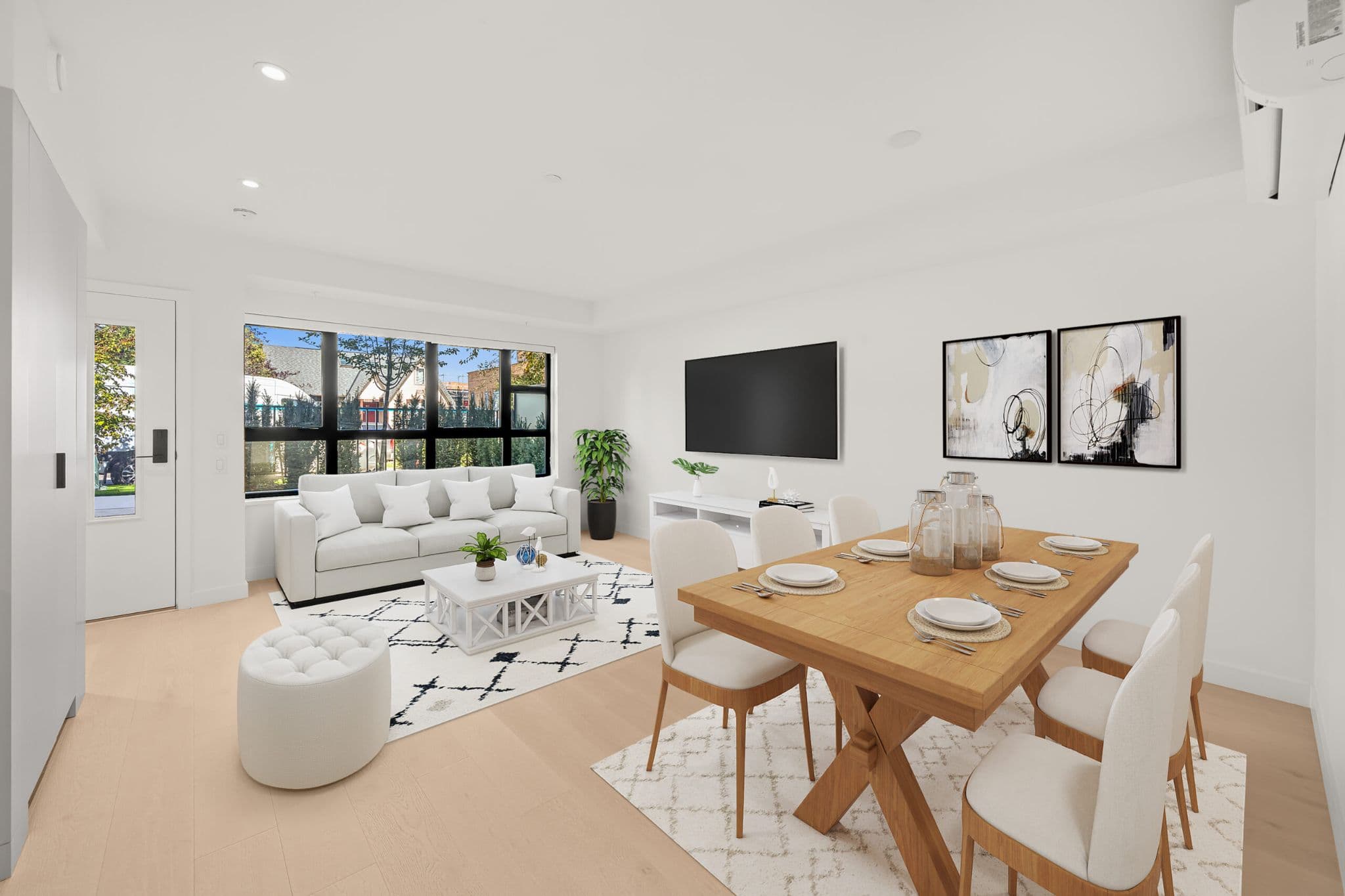 Lilibet – Open living and dining room with a white sofa, wall-mounted TV, framed abstract art, and a wood dining table set for eight.