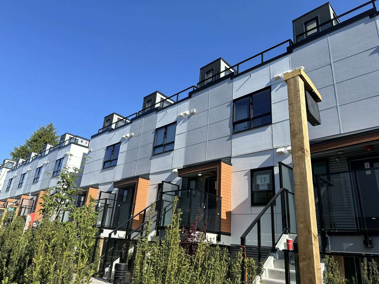 Lilibet – Street-level view down a row of grey-panelled townhomes with orange wood-look entry accents, rooftop decks, and unit number 17 visible on one entrance.
