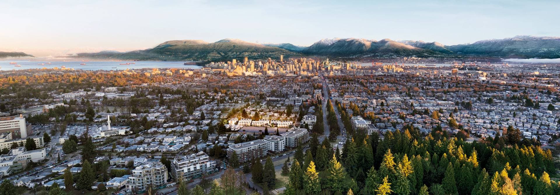 Lilibet – Aerial panorama at dusk showing downtown Vancouver's skyline and the North Shore mountains, with the townhome development highlighted amid a tree-lined residential neighborhood in the foreground.
