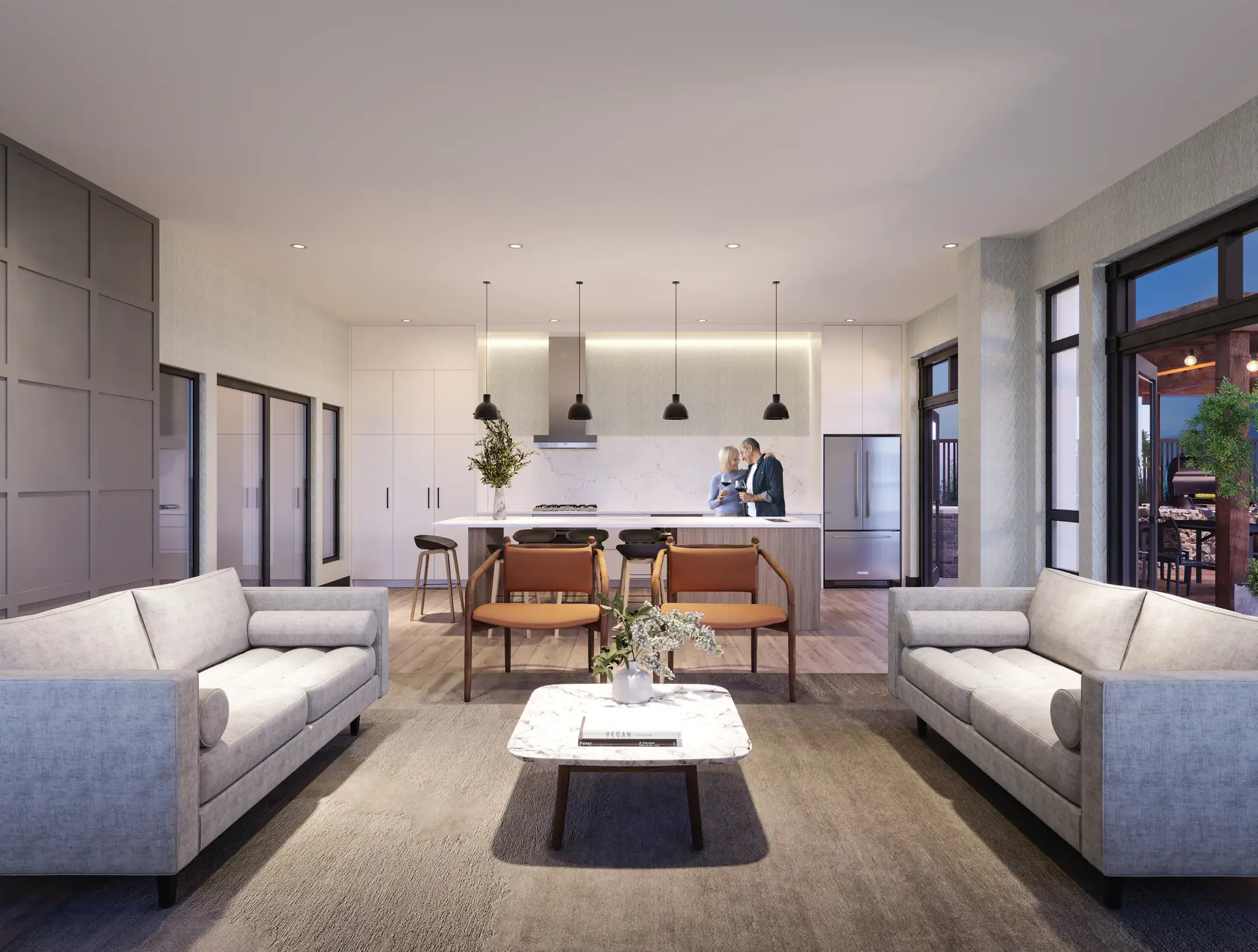 Terrayne Towns – An open-concept living and kitchen area features two plush grey sofas facing each other over a marble coffee table, with two leather armchairs positioned behind them. In the background, a modern kitchen with white cabinetry, stainless steel appliances, and black pendant lights overlooks an island where a couple stands holding wine glasses.