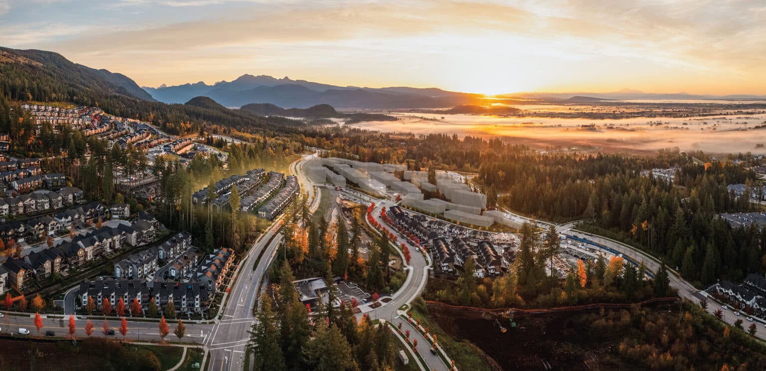 Terrayne Towns – An expansive drone view captures a hillside residential neighborhood nestled among autumn trees, winding roads, and mountain ranges. The golden morning sunrise casts a warm glow over low-lying fog blanketed across the valley floor.