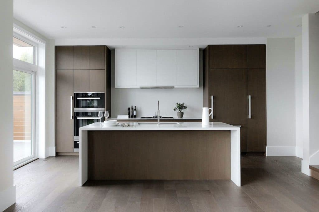 The Peak at Mulgrave Park – Modern kitchen with two-tone brown and white cabinetry, a waterfall-edge island, built-in oven, and gas cooktop.