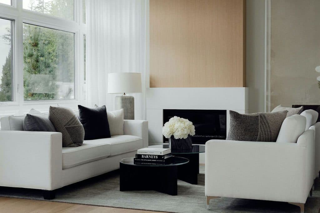 The Peak at Mulgrave Park – Living room with two white sofas, patterned throw pillows, a black coffee table, and a wood-panel accent wall above a gas fireplace.