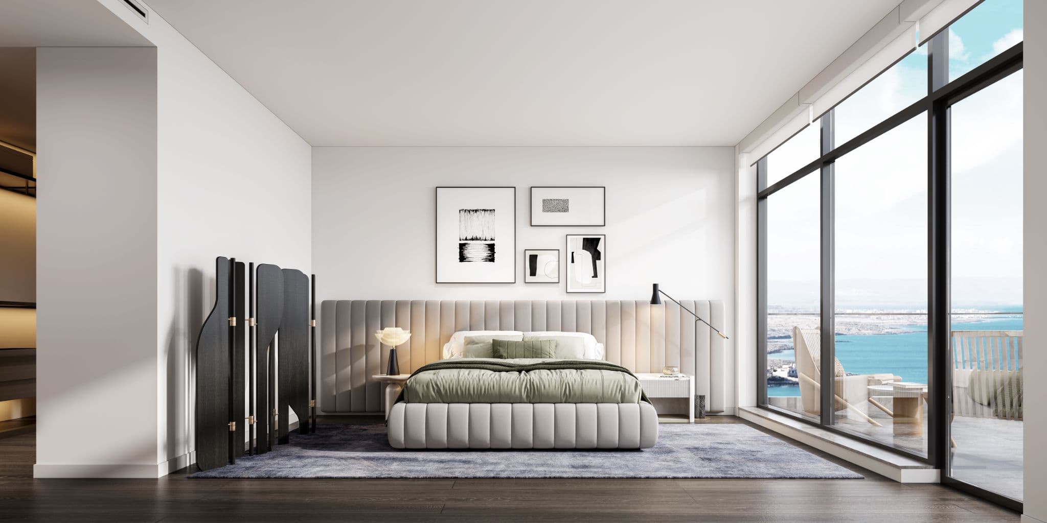 Rodgers Creek One – A modern, sunlit bedroom featuring a low-profile channel-tufted bed with sage green linens against a full-width upholstered headboard. Floor-to-ceiling windows line the right side, revealing a furnished balcony overlooking bright blue ocean waters and coastline.