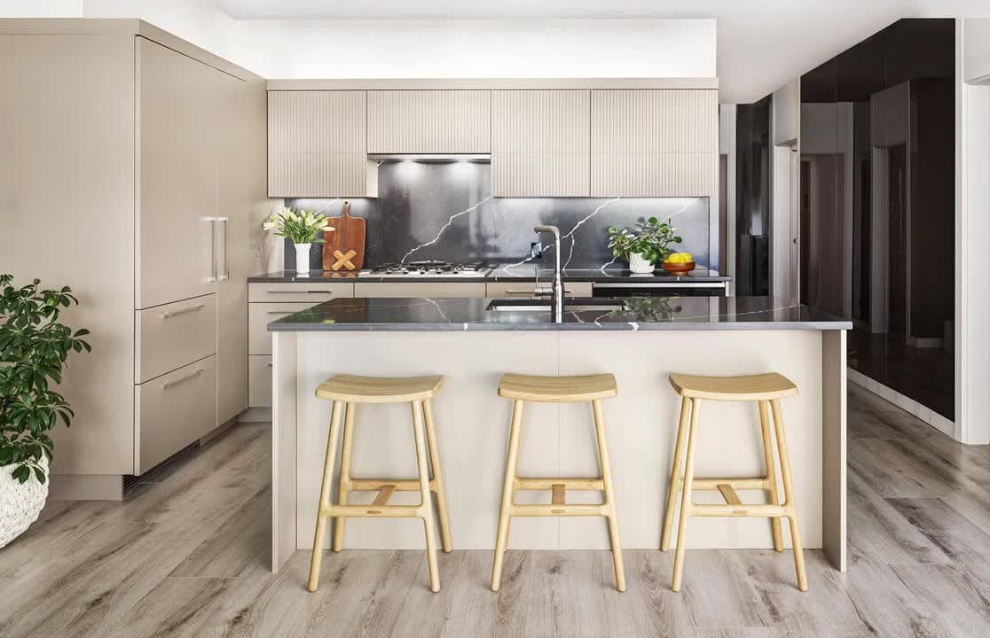 Circle at Concord Brentwood – Kitchen with beige cabinetry, a dark veined marble backsplash and island, and three light wood barstools.