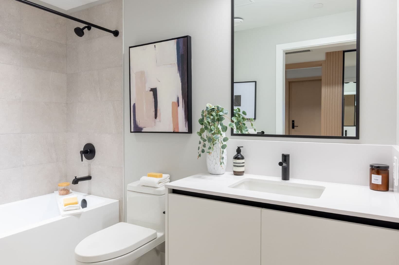 Umbra at Portwood – A modern bathroom featuring a white vanity with black hardware, a toilet, a bathtub, and neutral wall tiles.