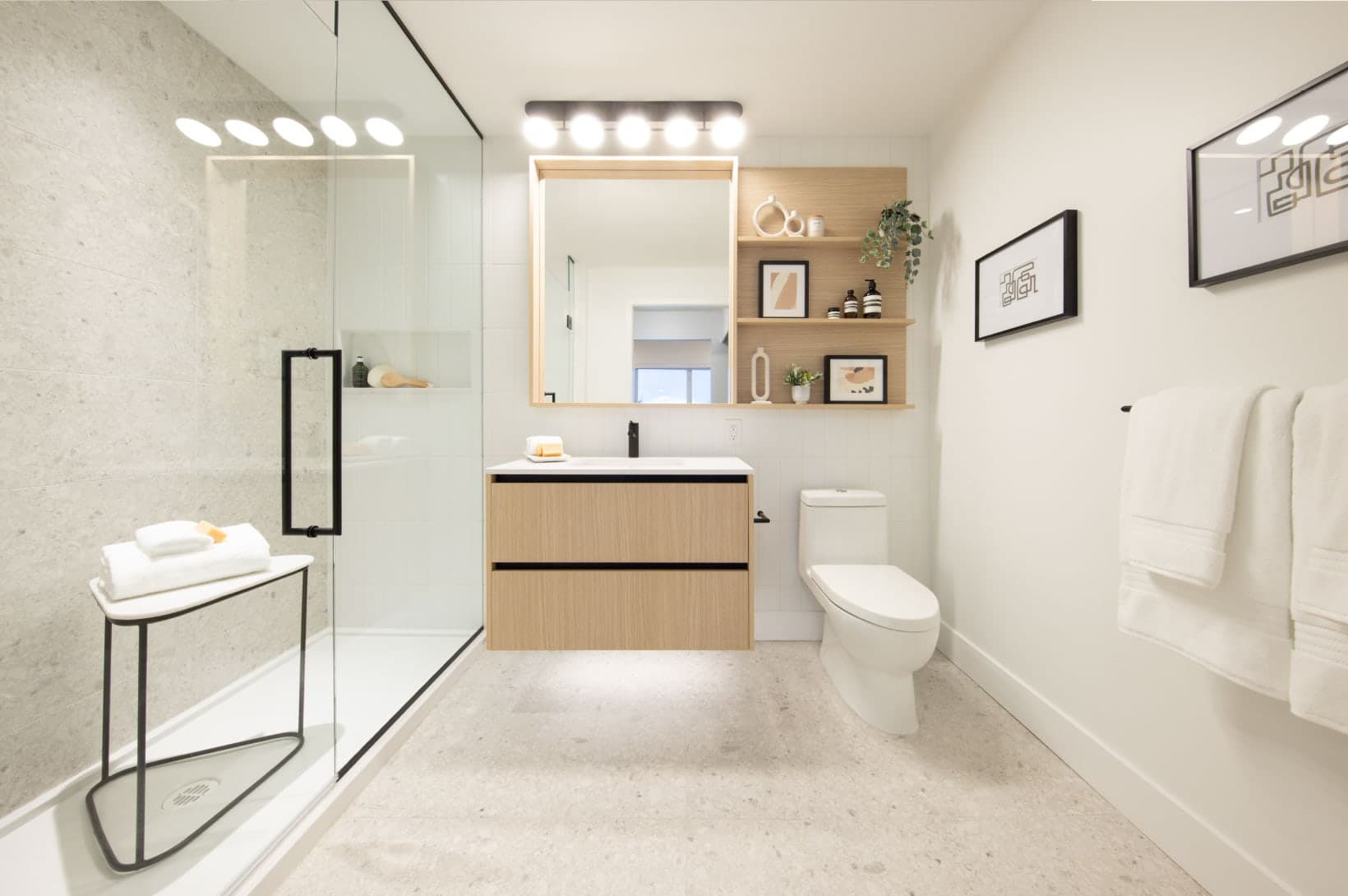 Umbra at Portwood – A bright bathroom with a floating light-wood vanity, toilet, and glass shower enclosure.