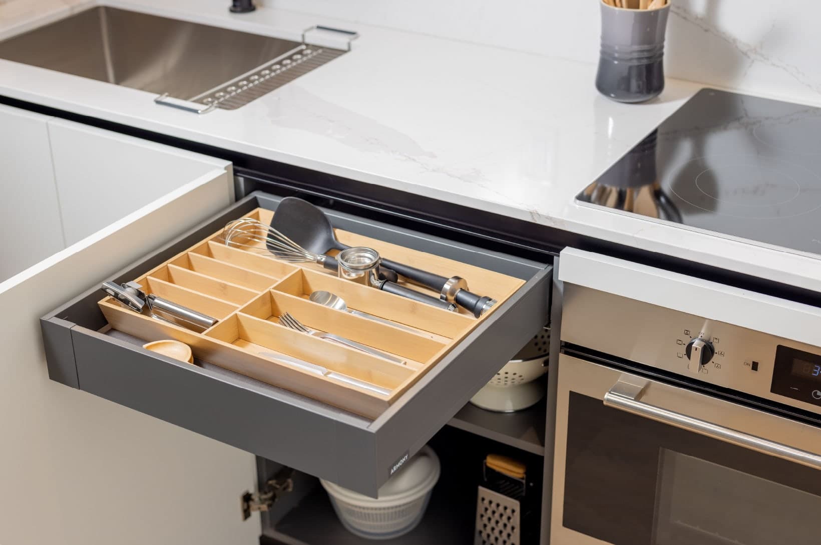 Umbra at Portwood – Close-up of a modern kitchen drawer with a built-in wooden organizer alongside an induction cooktop and oven.