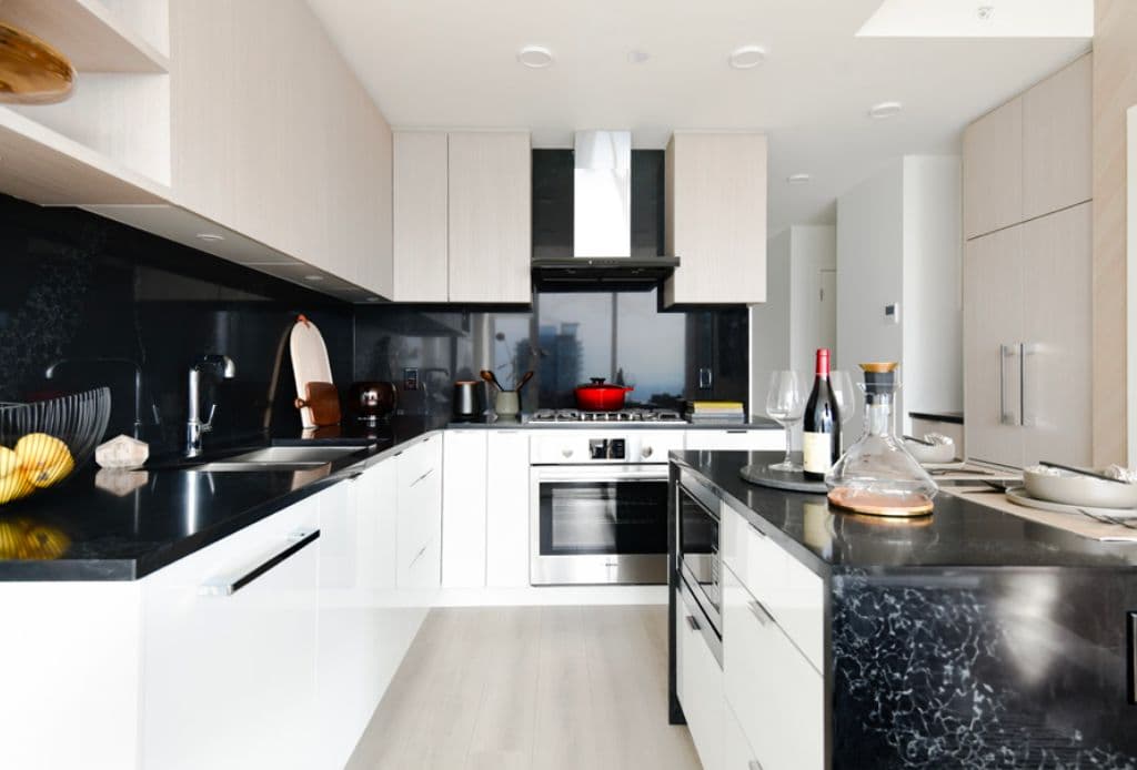 Riviera – Modern kitchen with two-tone light wood and white cabinetry, black stone countertops and backsplash, stainless appliances and an island.