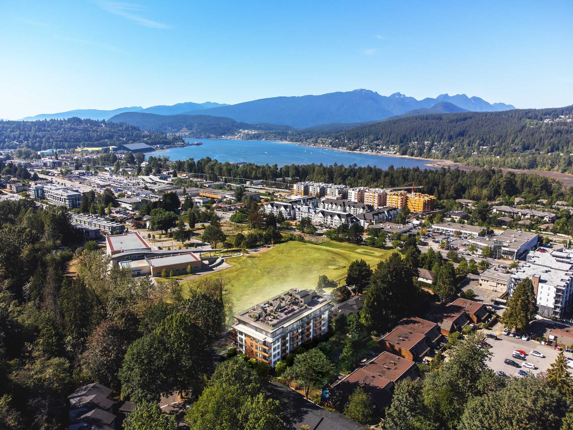 Sitka House – Overhead drone view of the low-rise building site next to Burrard Inlet, with mountains in the background and surrounding neighborhood buildings.