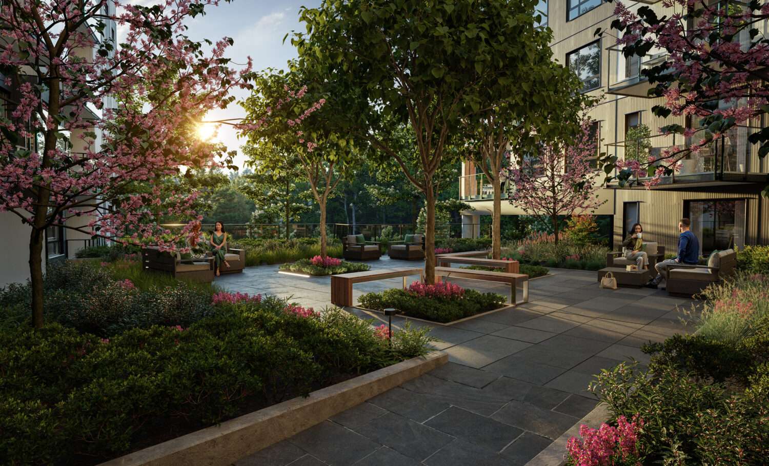 Emerald – A lush outdoor courtyard and terrace bathed in warm afternoon sunlight, featuring stone pavers, wooden benches, and comfortable lounge seating areas. Flowering cherry blossom trees, leafy green foliage, and landscaped garden beds surround the residents enjoying the serene environment adjacent to modern residential buildings.