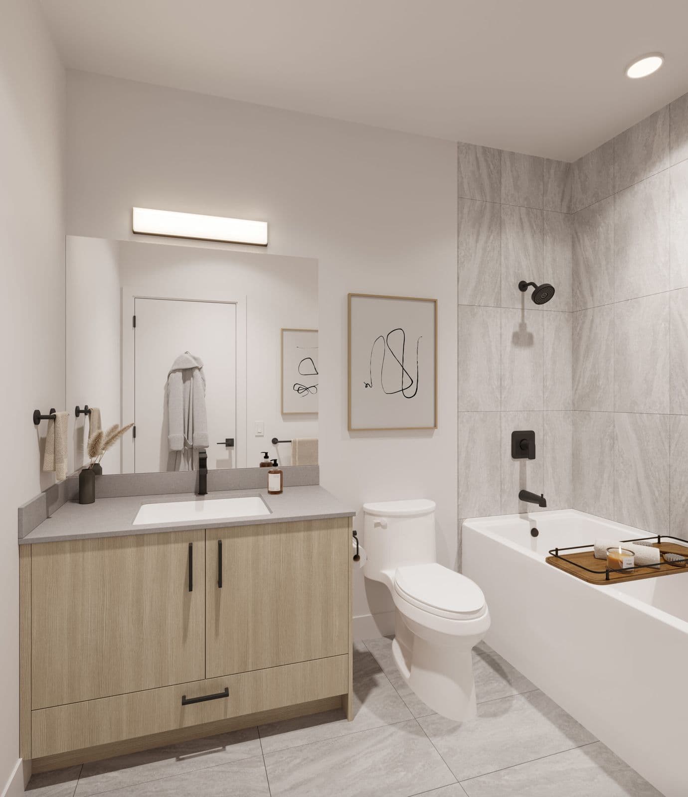 The Commons – Bathroom with a light wood vanity, grey countertop, large mirror, and a separate tub/shower combo with grey tile surround.
