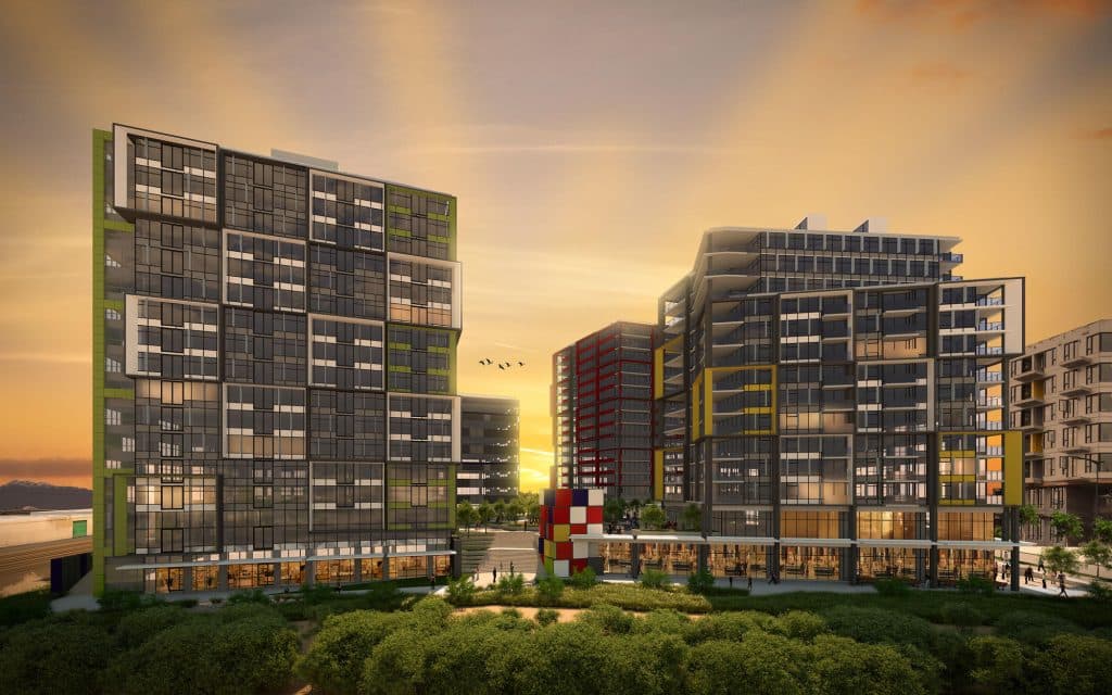 375 East 1st Avenue Condos – A architectural rendering of multiple mid-rise modern residential buildings featuring glass facades with green, yellow, and red exterior accents set against a golden sunset sky. Ground-level retail spaces look out onto landscaped green areas and a central pedestrian plaza with a colorful public art installation.