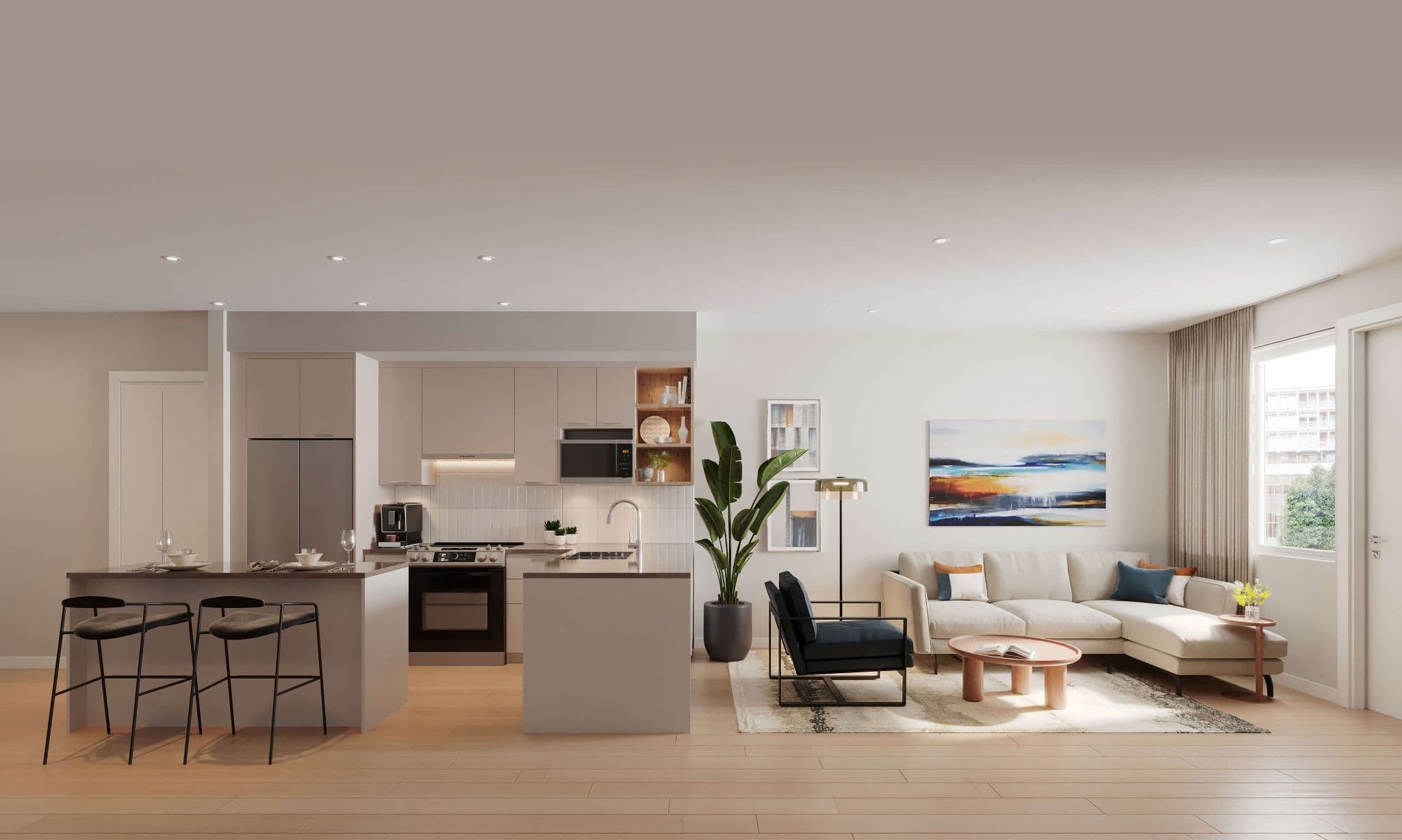 Stowa – An open-concept condo interior showcasing a modern kitchen with flat-panel cabinetry, stainless steel appliances, and a kitchen island with bar seating, leading directly into a bright living room. The space is styled in neutral tones with light wood flooring, a beige sectional sofa, colorful artwork, and a large indoor plant near the window.