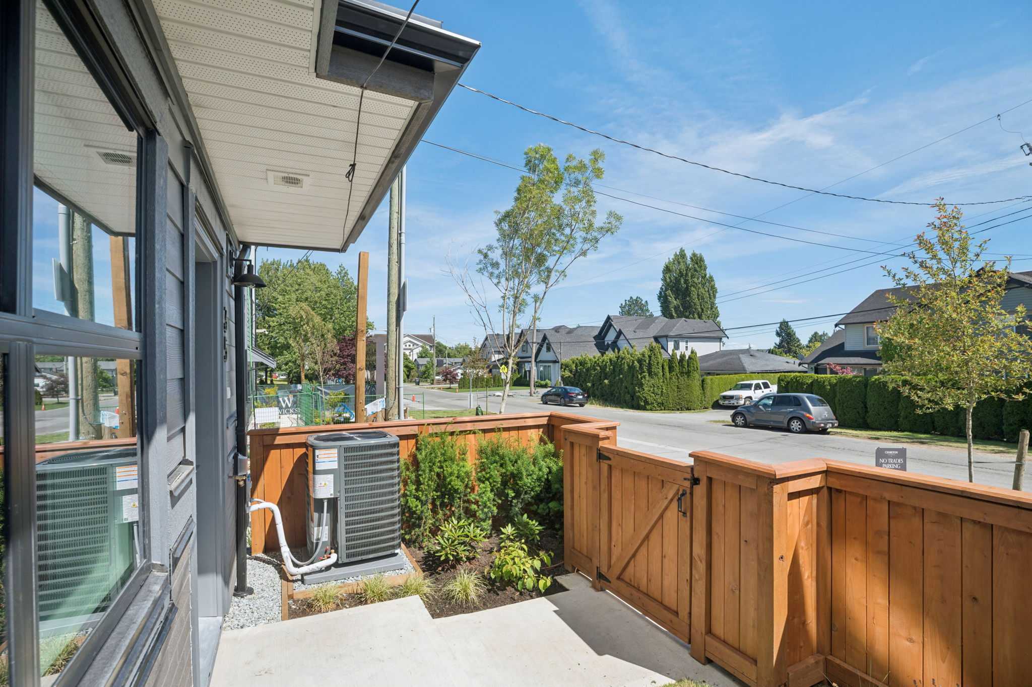 Charlton – Ground-level patio area with an AC condenser unit, wood privacy fence with gate, and view to the street with parked cars.