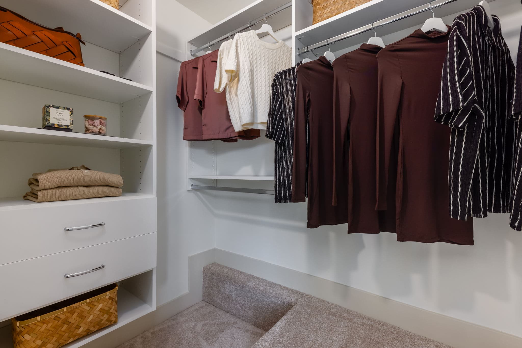 Charlton – Walk-in closet with white shelving, woven baskets, handbags, and hanging clothes including sweaters and dresses on rods.