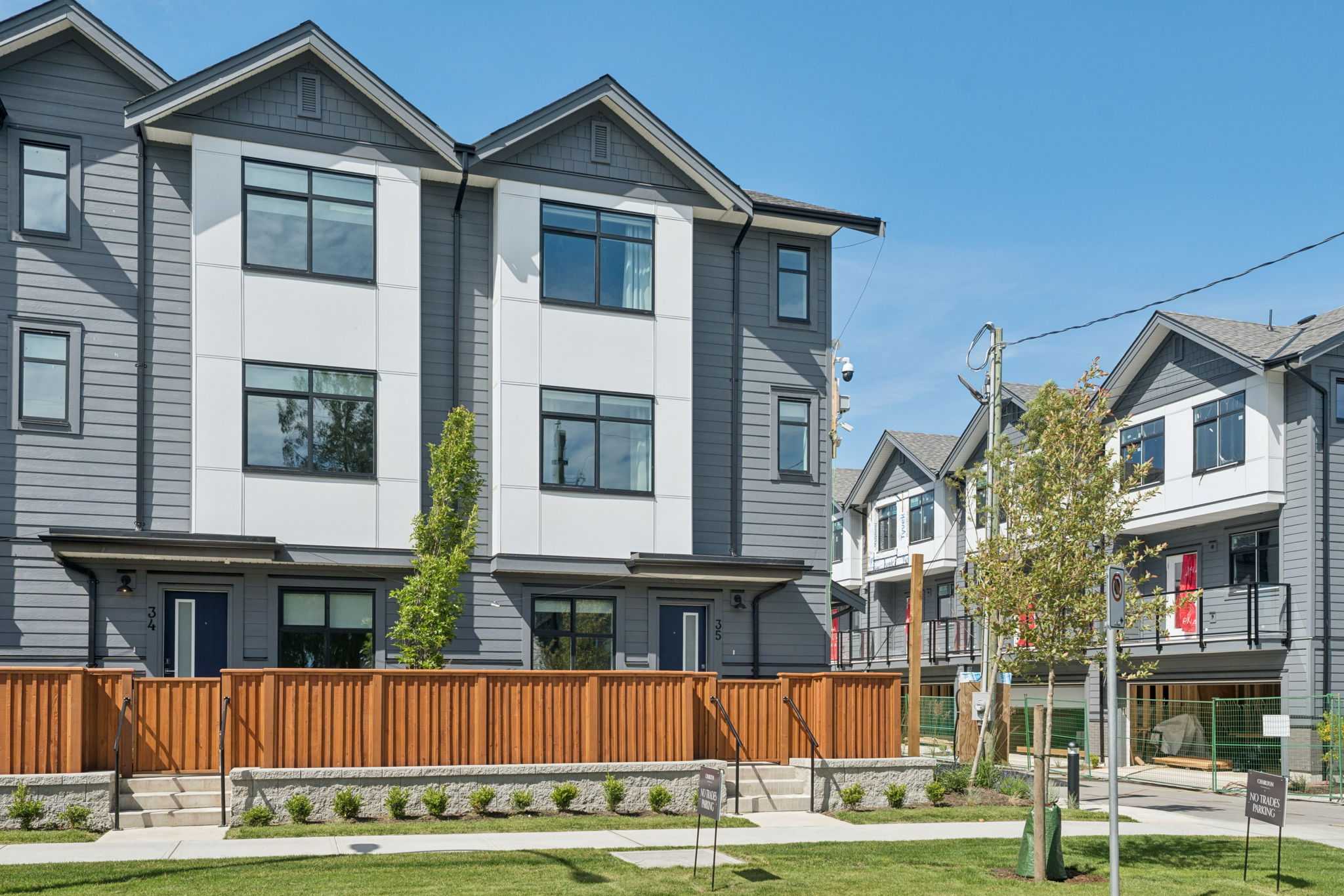 Charlton – Three-storey grey and white townhomes with peaked rooflines, black-framed windows, and a wood privacy fence along the front walkway.