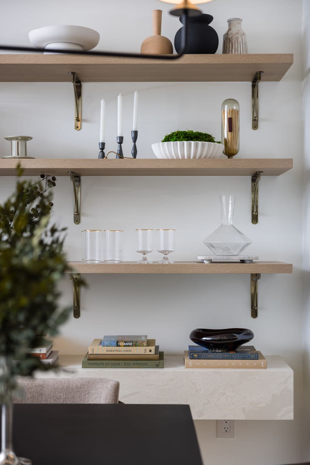Charlton – Close-up of open wood shelving displaying candles, vases, glassware, a decanter, and stacked books on a floating shelf below.