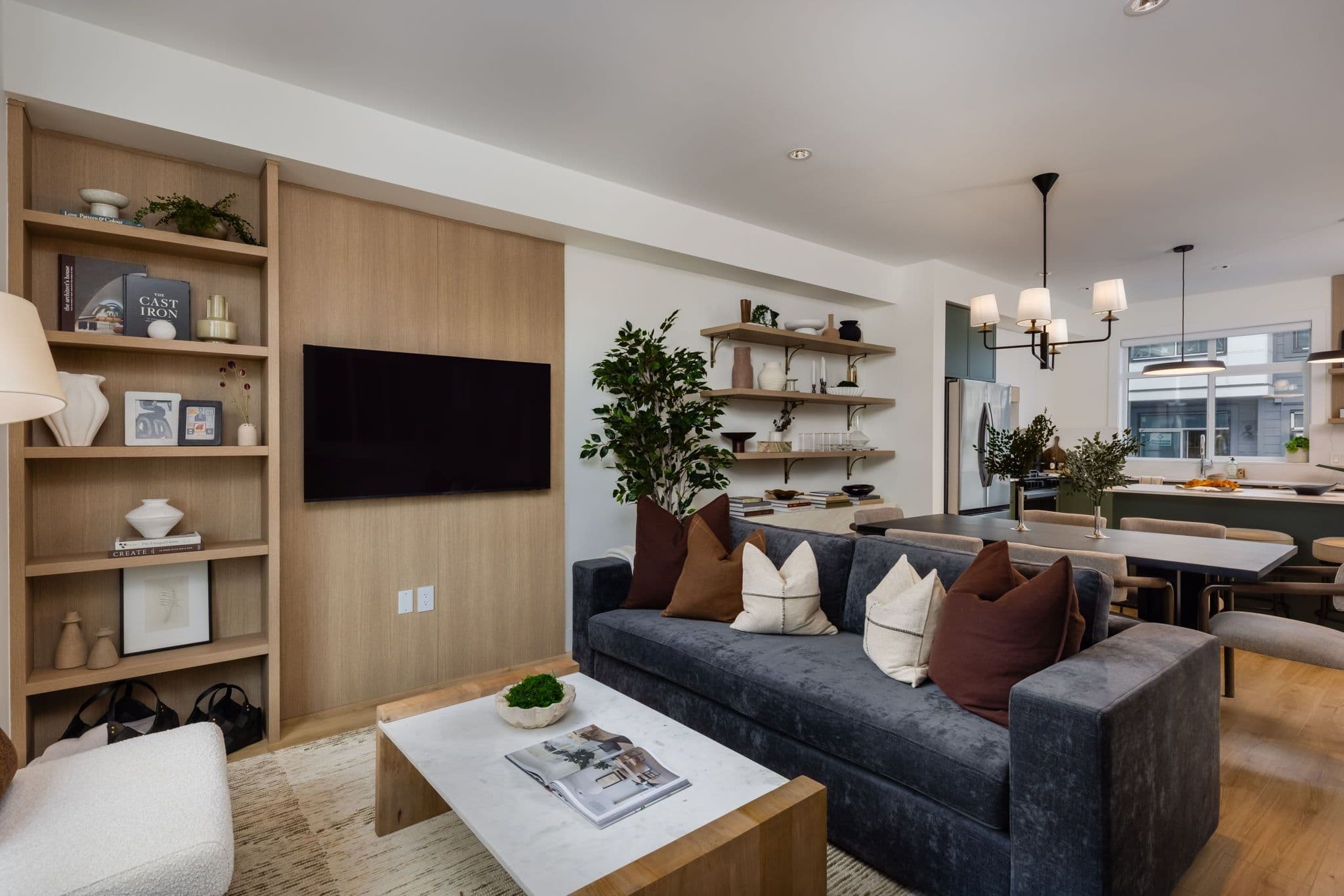 Charlton – Open-concept living room with wood-panel TV wall, built-in bookshelf, and a view through to the dining table and kitchen.