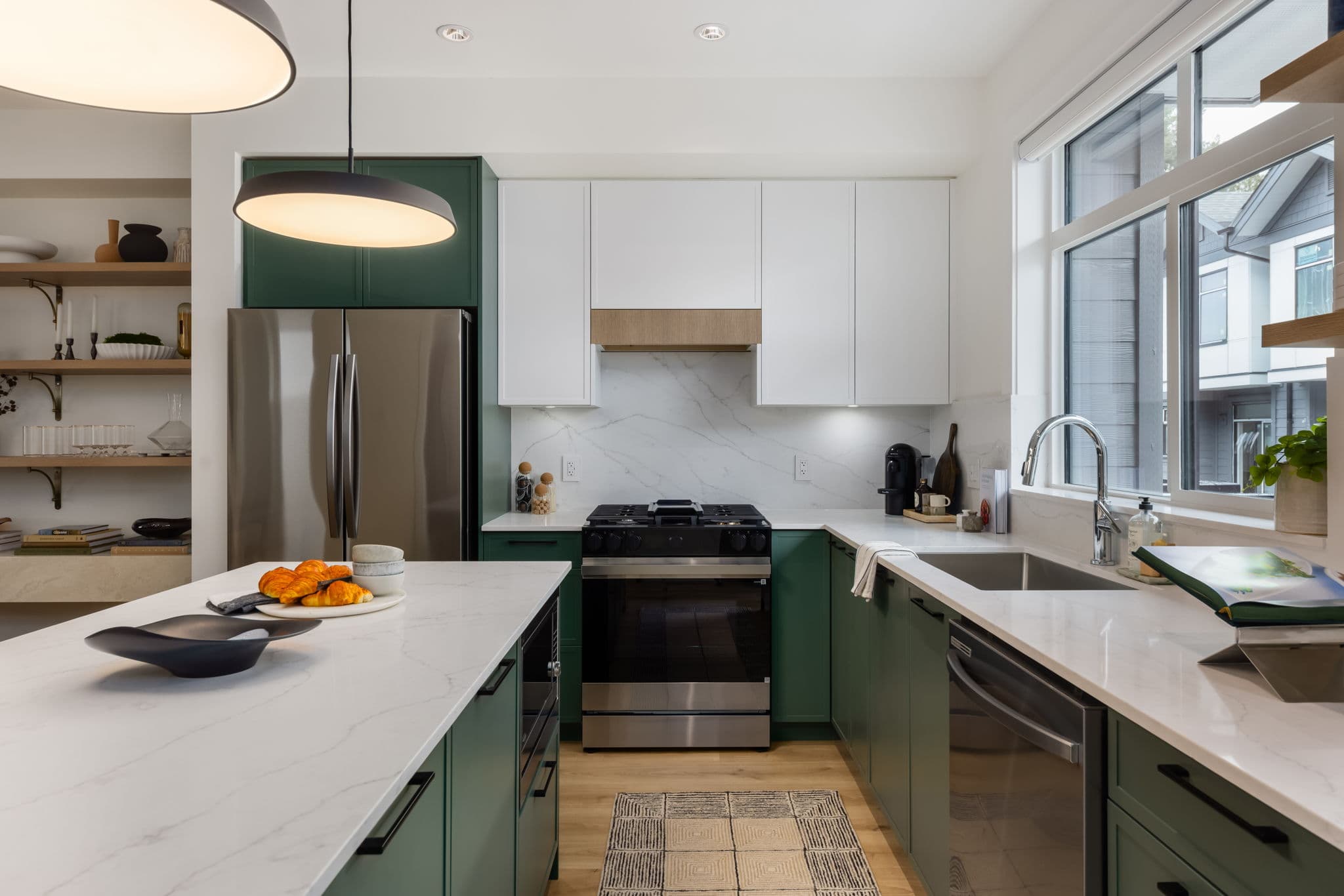 Charlton – Kitchen with dark green cabinetry, white uppers, stainless fridge and gas range, marble backsplash, and open wood shelving.