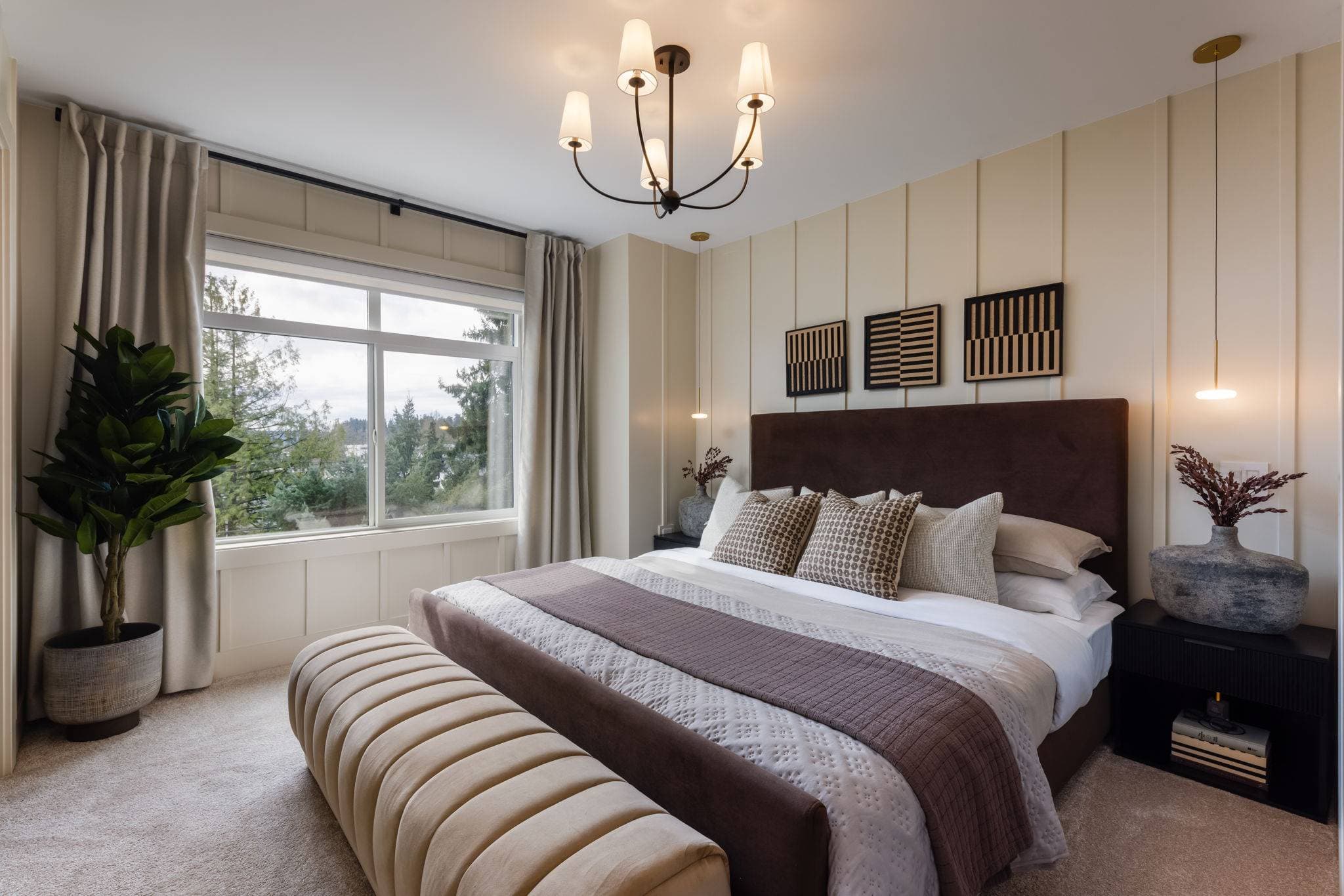 Charlton – Primary bedroom with cream paneled walls, a dark brown upholstered headboard, patterned pillows, and abstract framed wall art.