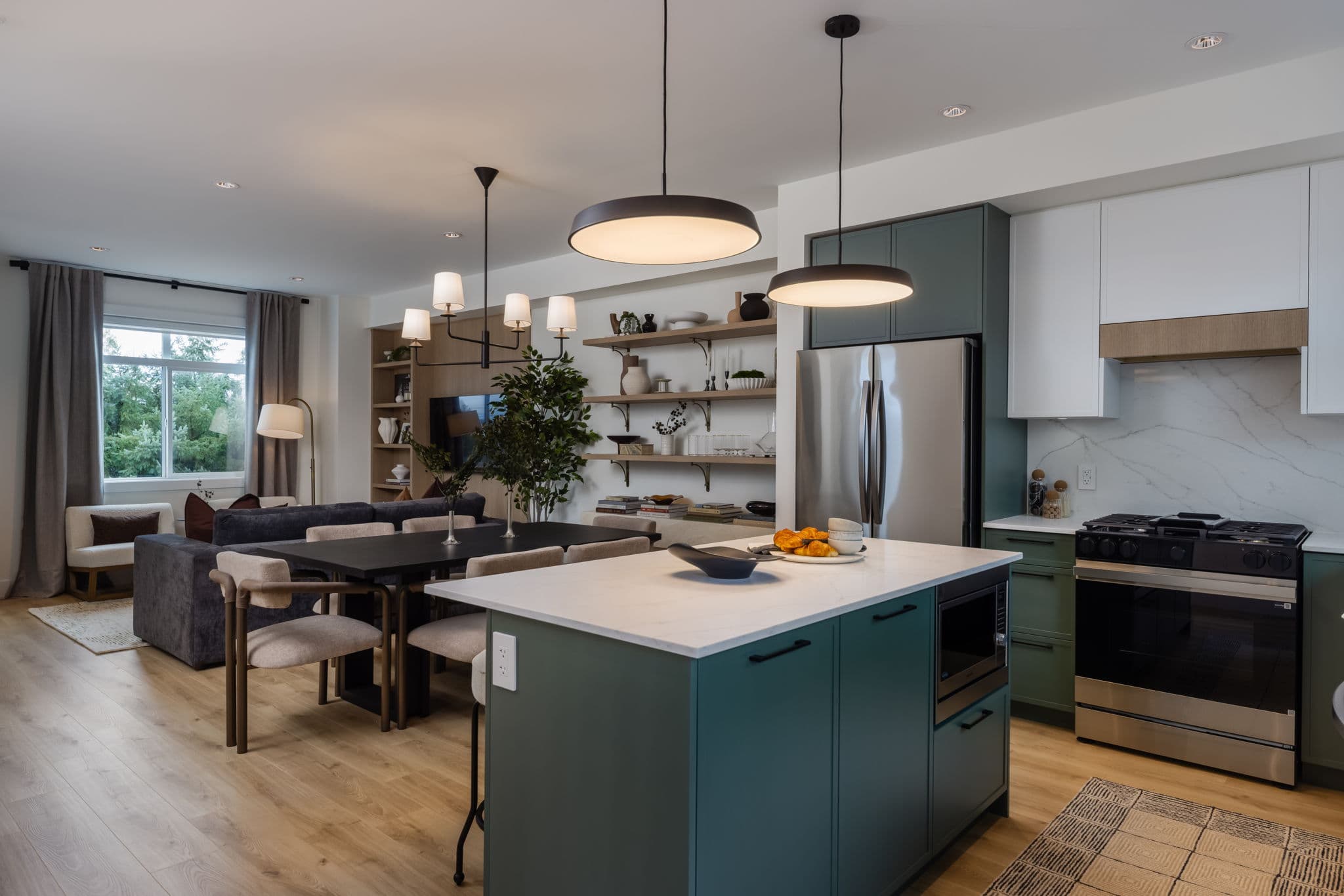 Charlton – Kitchen with green island seating three stools, marble countertop with croissants, black pendant lights, and stainless fridge.