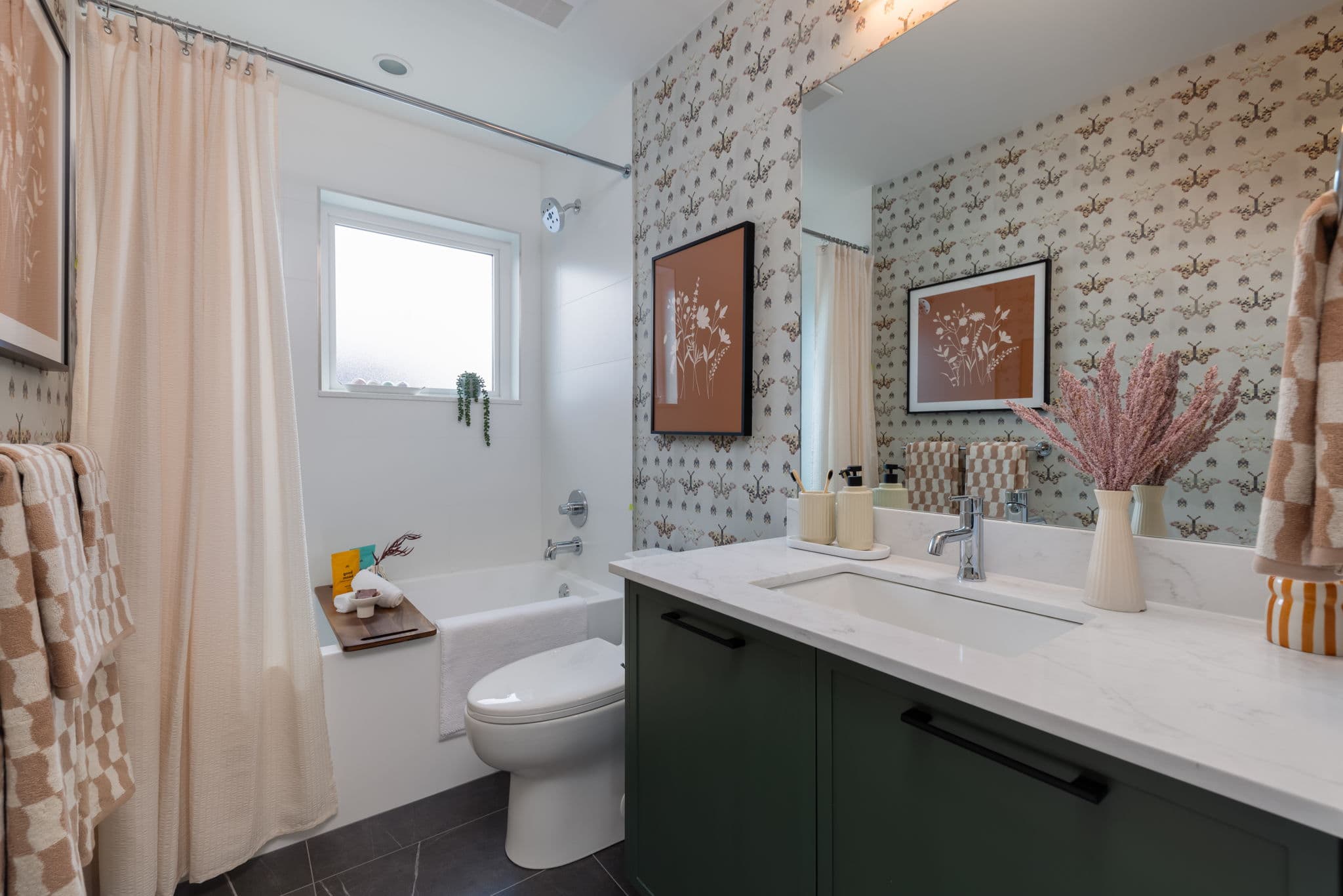 Charlton – Bathroom with butterfly-print wallpaper, a green vanity with white marble counter, tub with shower curtain, and framed floral art.