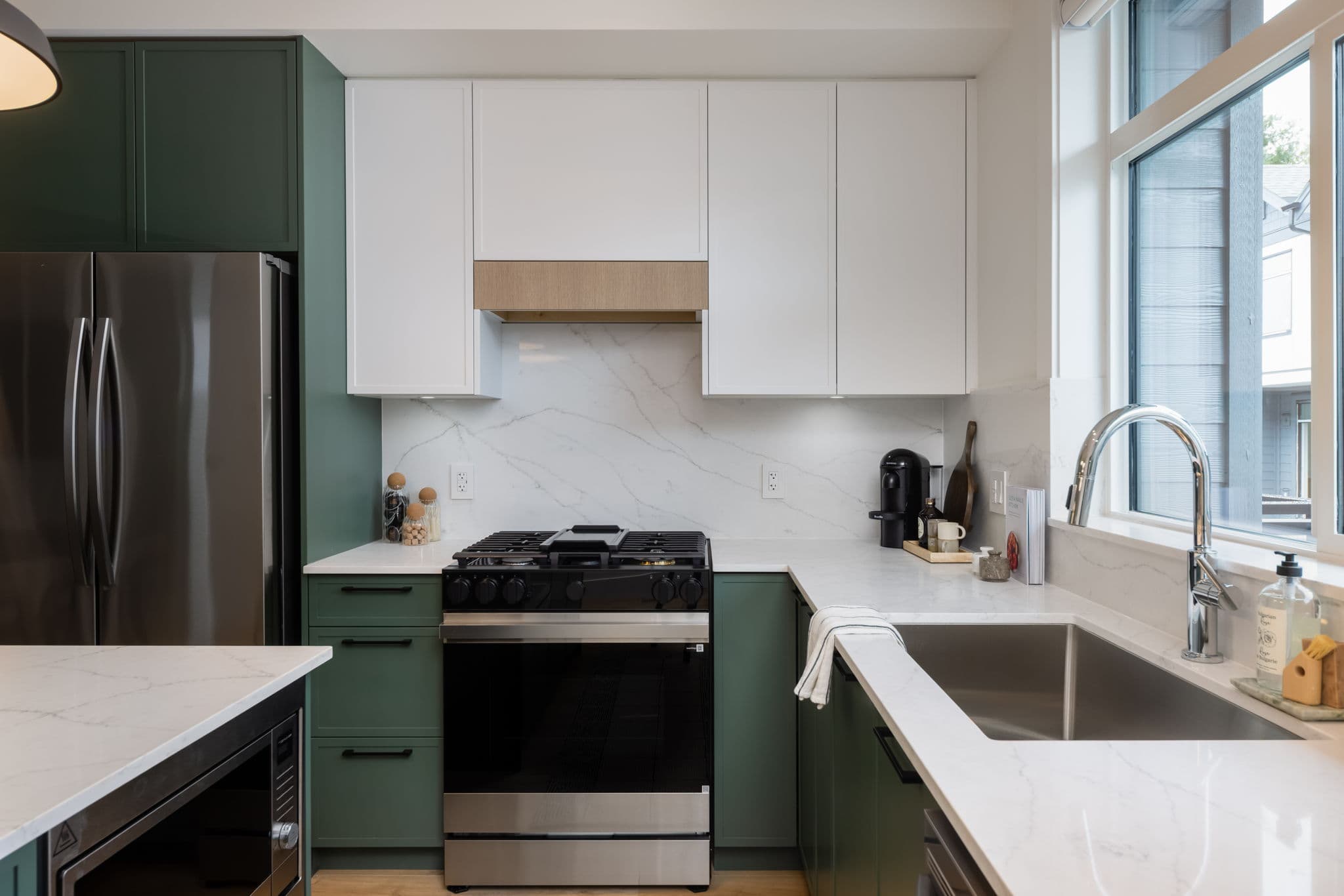 Charlton – Close-up of a kitchen gas range and marble backsplash flanked by green lower cabinets and white upper cabinets.
