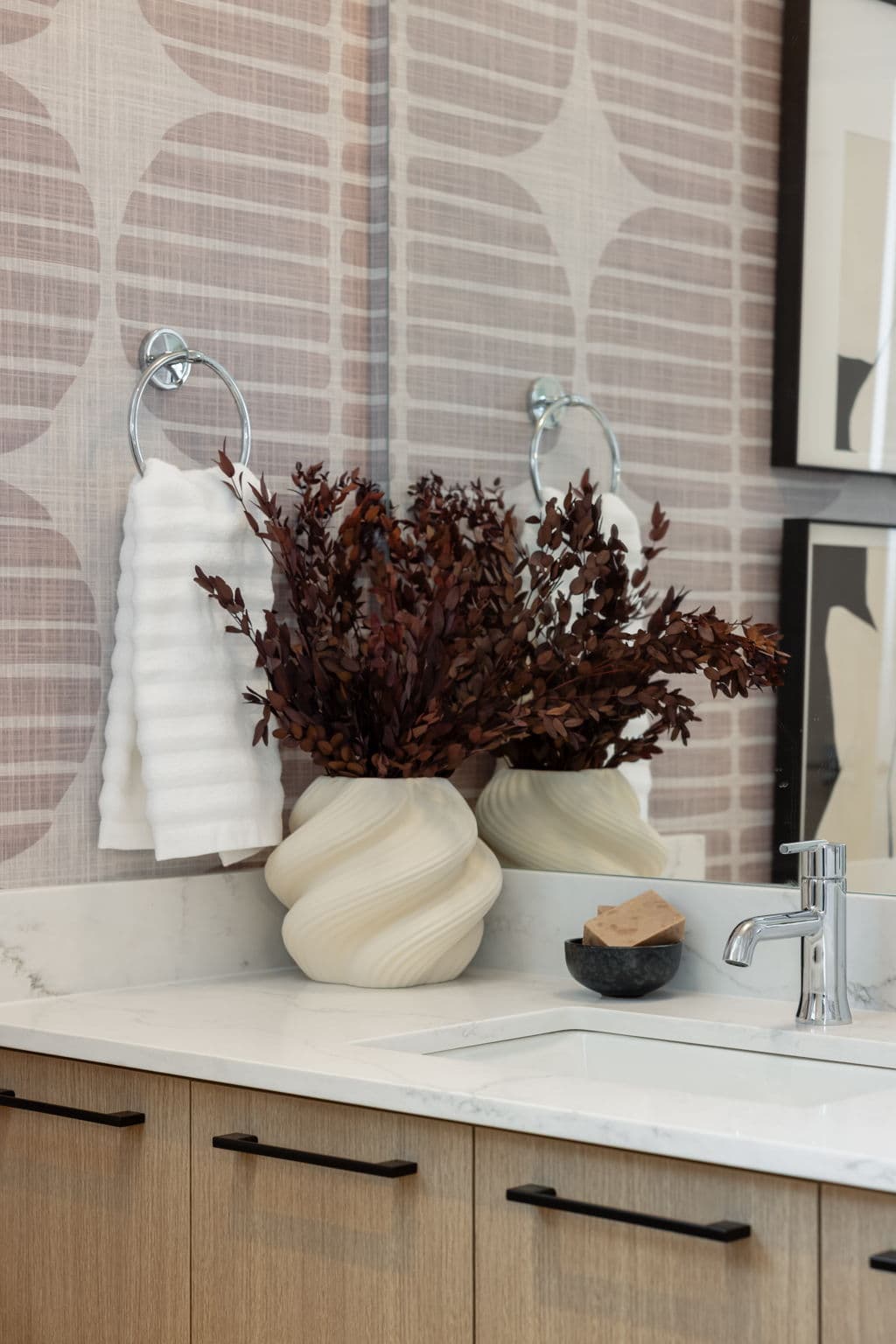 Charlton – Close-up of a bathroom vanity with two swirled ceramic vases holding dried branches, a soap dish, and chrome faucet.