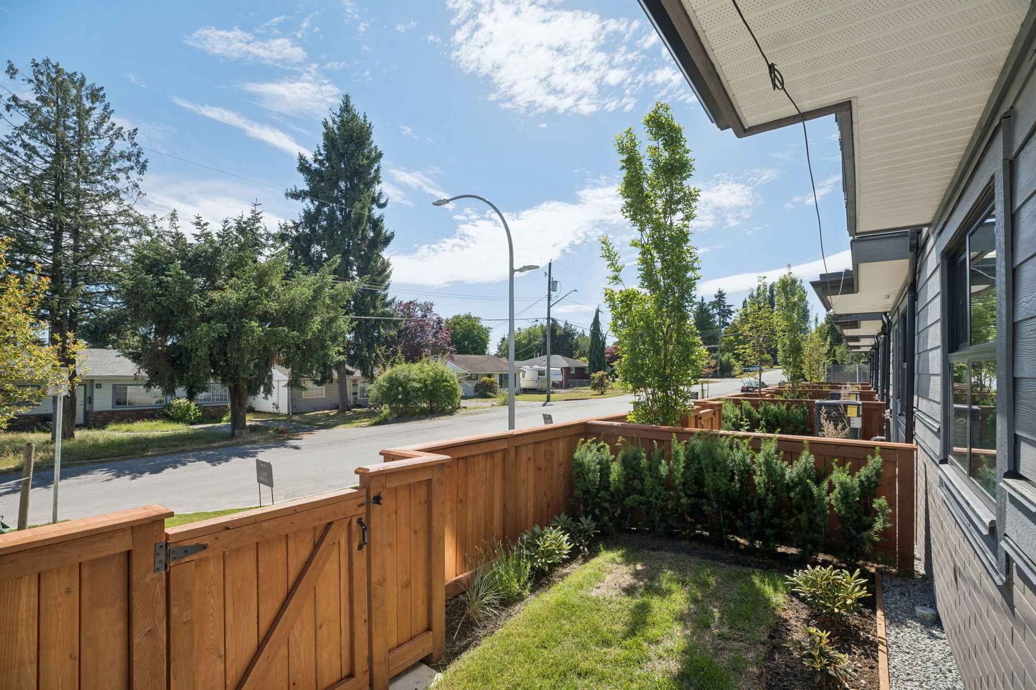 Charlton – View from a ground-floor unit's fenced patio out to a residential street lined with trees, showing the wood privacy fence and siding.