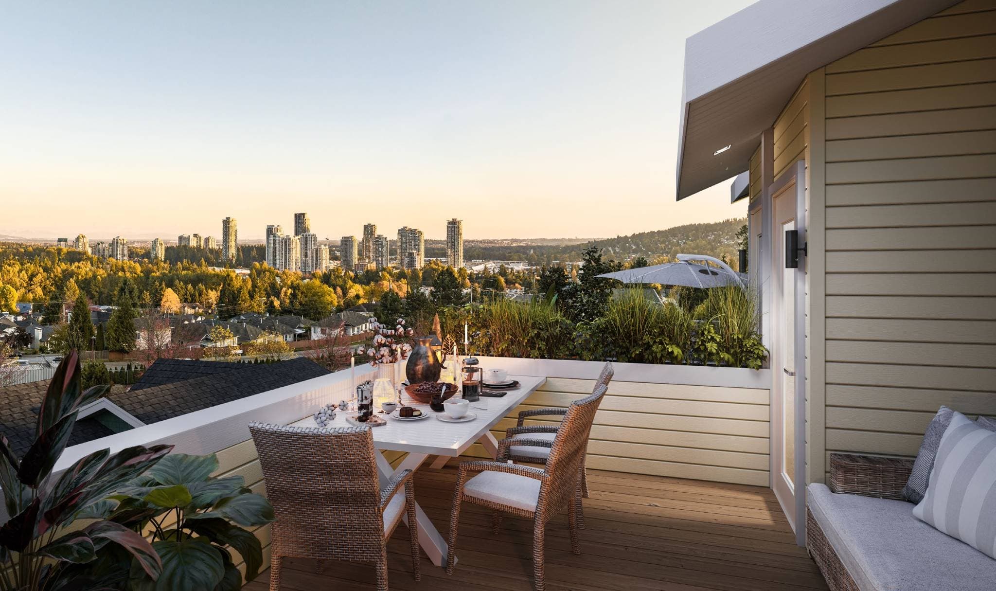 Westview Townhomes – A rooftop balcony furnished with a set dining table and outdoor lounge seating overlooks an expansive view of lush green tree canopies and a distant high-rise city skyline. Soft golden hour light fills the clear sky, highlighting the warm wood decking and potted greenery along the railings.