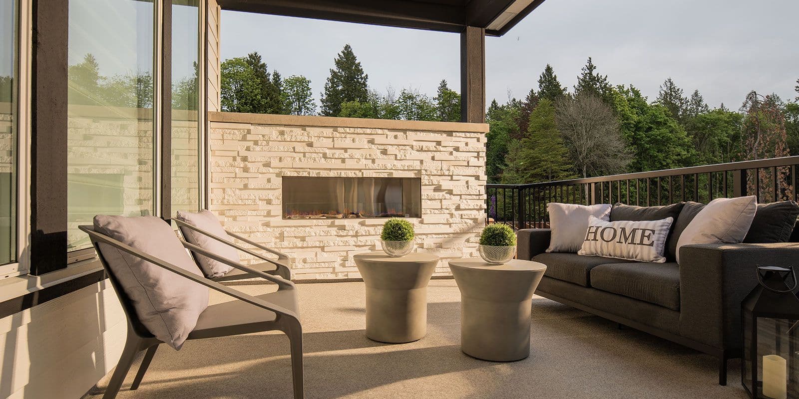 James Hill – Covered rooftop or upper-deck lounge with a built-in stone fireplace, outdoor sofa and lounge chairs, overlooking treetops.