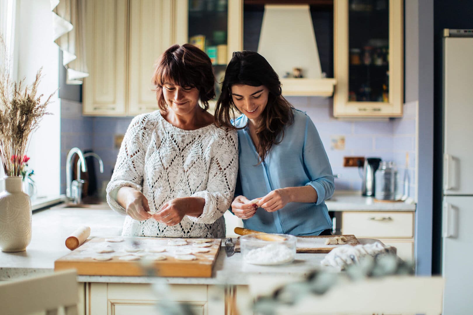 James Hill – Lifestyle stock photo of two women baking together in a kitchen, rolling dough on a wooden board.