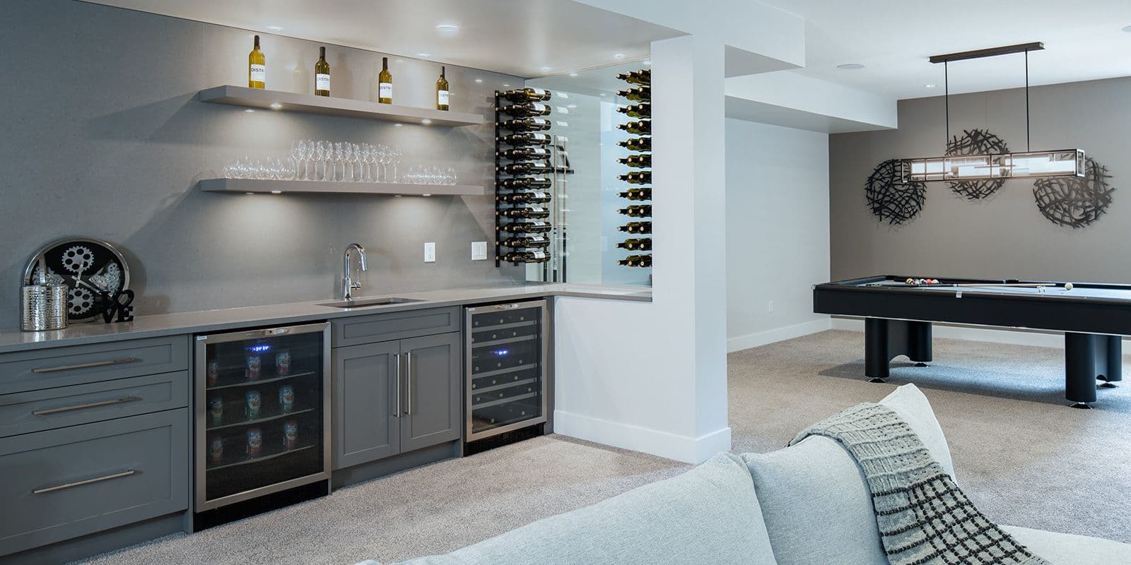 James Hill – Basement rec room with a built-in wet bar, glass-front beverage fridges, a wine display wall, and a pool table in the background.
