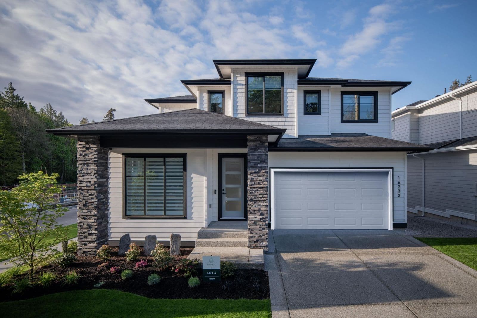 James Hill – Two-story modern home with white siding, dark trim, stone-clad entry columns, and an attached two-car garage, photographed in daylight.