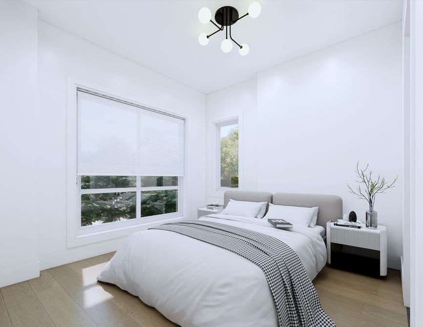 Clove – A bright, minimalist bedroom features a bed dressed in crisp white linens and a patterned throw blanket beneath a modern multi-bulb ceiling fixture. Large windows with semi-translucent blinds overlook outdoor greenery, filling the white-walled room with soft daylight onto light hardwood floors.