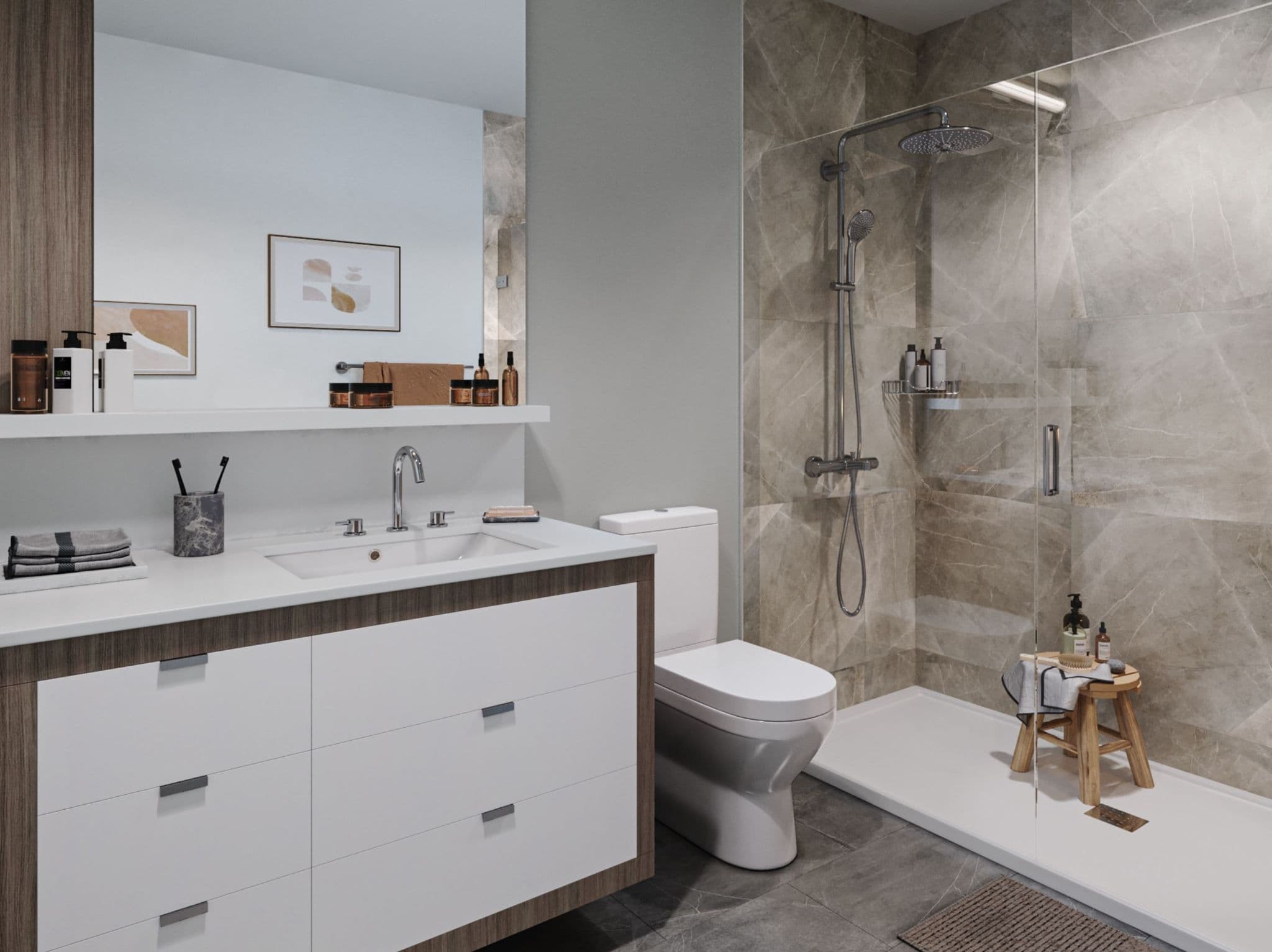 Luxio on the Park – A modern ensuite bathroom featuring a white floating vanity with wood trim, framed by a large mirror and neutral grey tiled floors. To the right, a walk-in shower with glass doors showcases full-height stone-look wall tiles, a rain showerhead, and a small wooden accent stool.