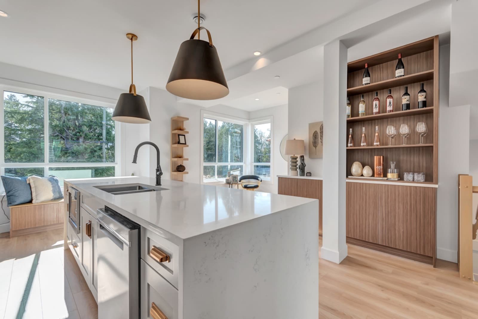 VIVID Townhomes – Kitchen island with wood pendant lighting and stainless fridge, next to a built-in wood shelving nook displaying wine bottles and glassware.