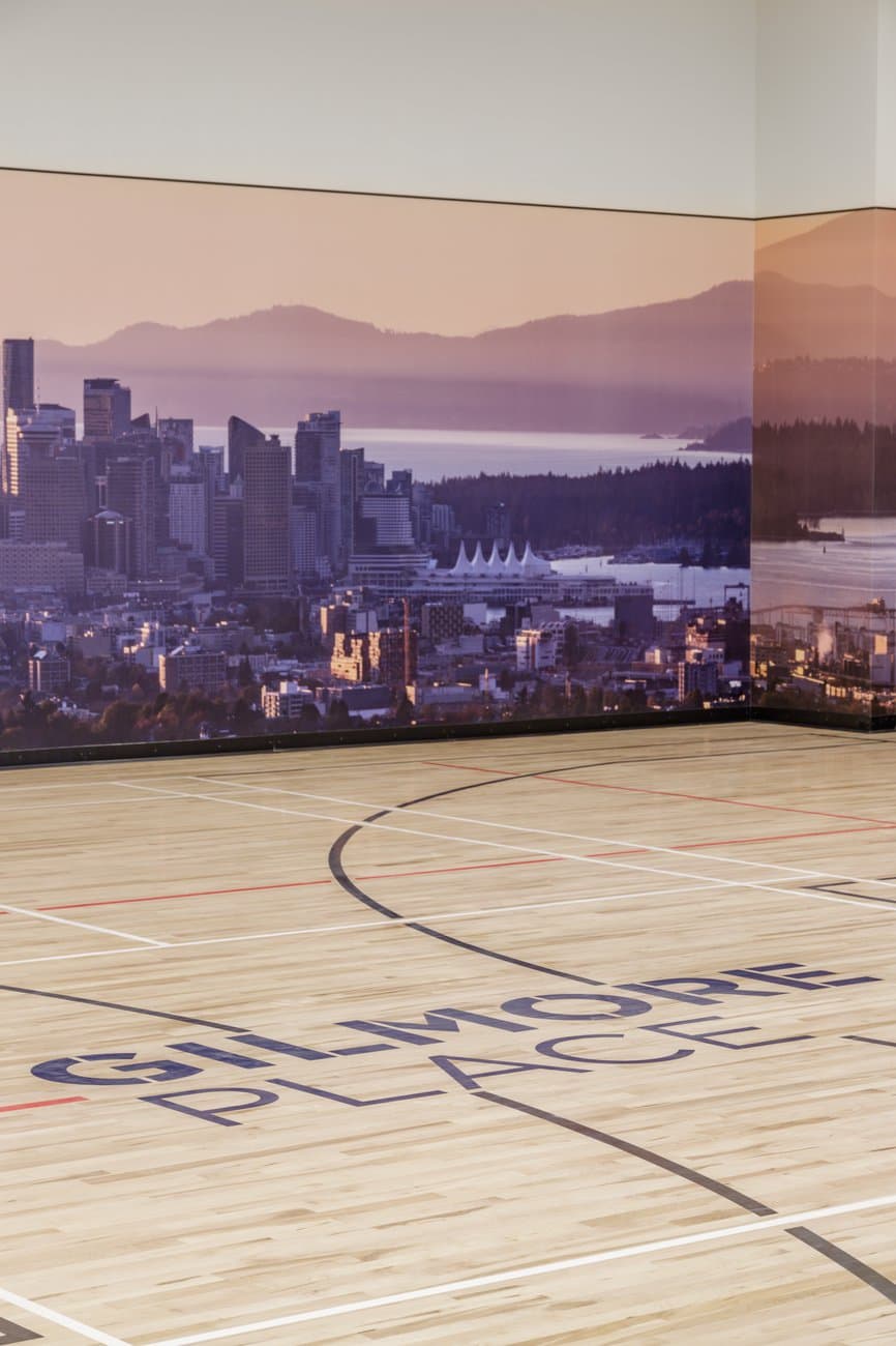 Gilmore Place Condos – Indoor sports court with the Gilmore Place logo painted on the wood floor and a large mural of the Vancouver skyline and mountains on the wall.