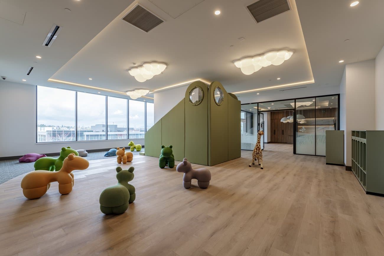 Gilmore Place Condos – Children's play lounge with soft animal-shaped seating, cloud-style ceiling lights, and a slide built into a padded green structure.
