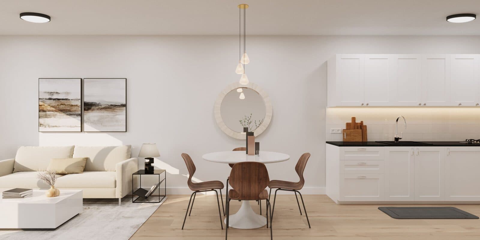 Orchard – A bright, open-concept living, dining, and kitchen space with light hardwood floors and crisp white walls. A small round dining table with wooden chairs sits centered between a cream-colored sofa setup on the left and white shaker-style kitchen cabinetry with black countertops on the right.