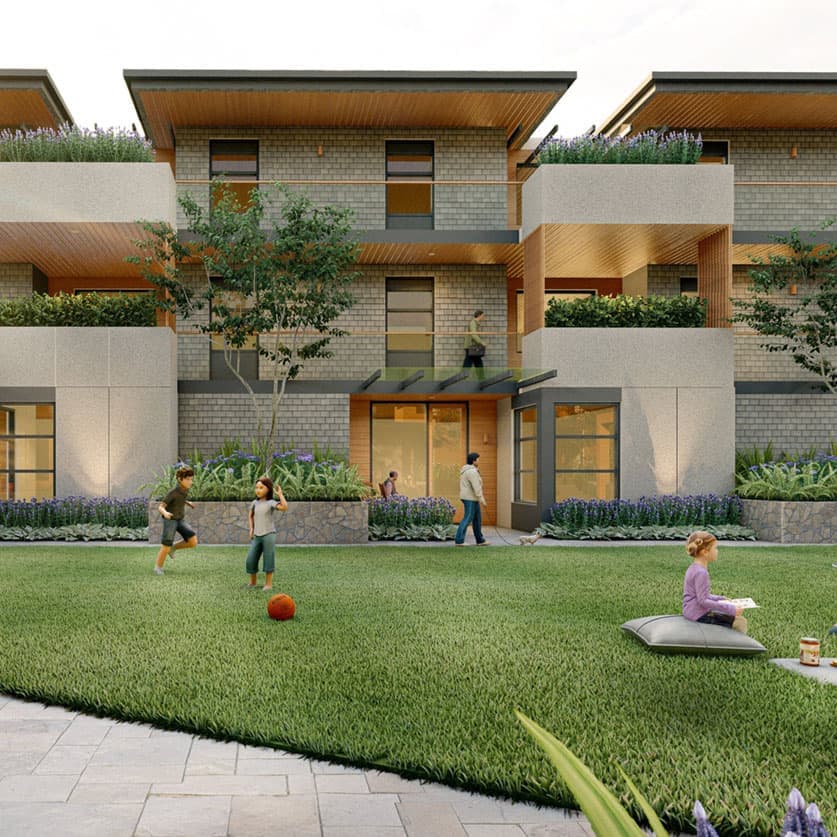 Compass Cohousing – Ground-level shared lawn between townhome units with children playing with a ball and a person relaxing on a floor cushion, entry doors visible behind.