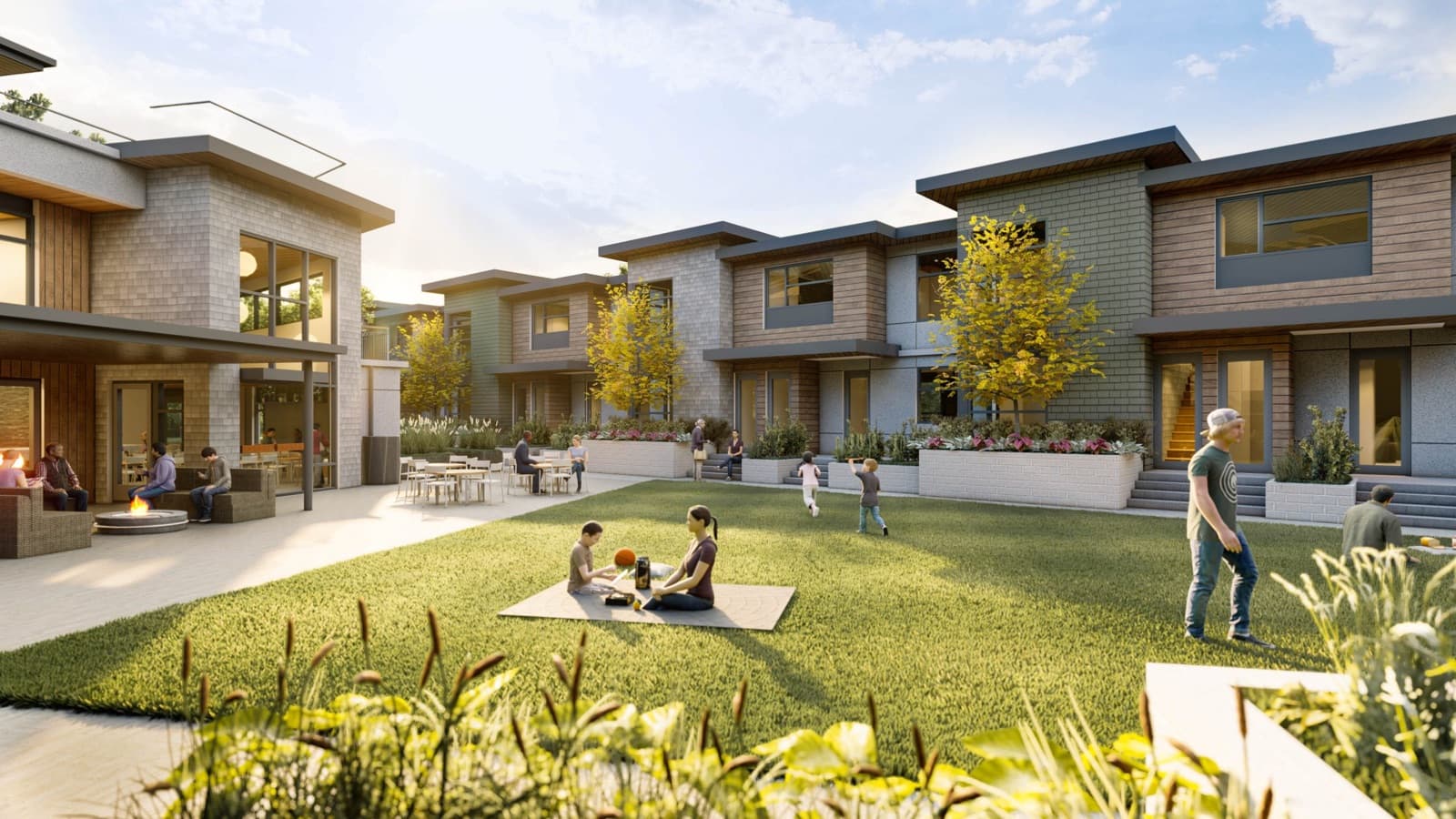 Compass Cohousing – Shared courtyard lawn between townhome buildings with residents relaxing on a picnic blanket, children playing, and a covered lounge with a fire pit.