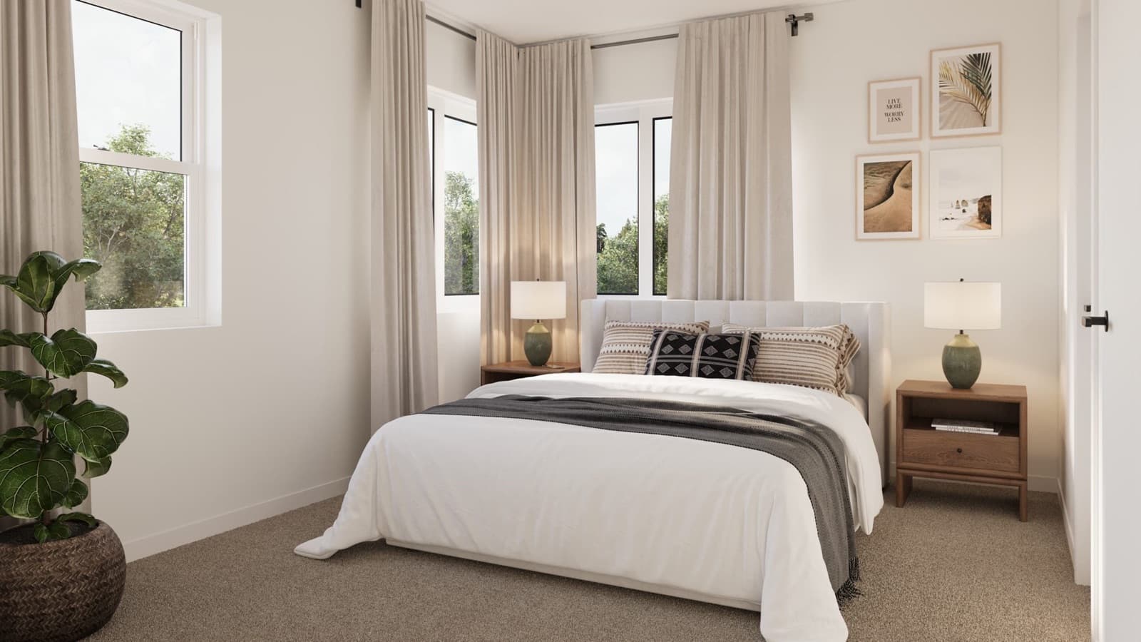 Compass Cohousing – Bedroom with a light grey upholstered bed, patterned throw pillows, corner windows with sheer curtains, and a potted fiddle leaf fig.