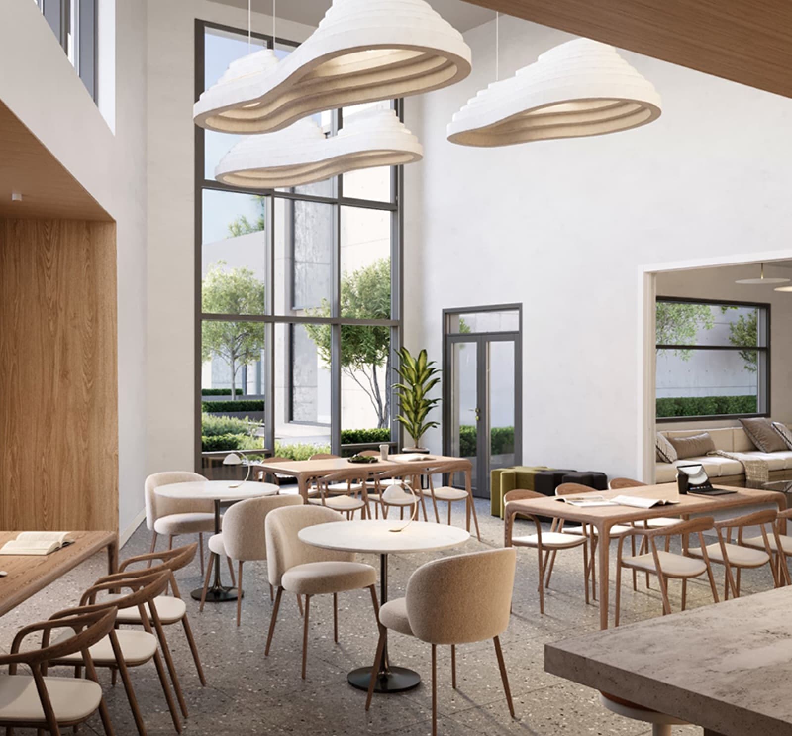 Compass Cohousing – Double-height shared lounge and dining commons with sculptural cloud-like pendant lights, communal tables, and floor-to-ceiling windows onto a courtyard.