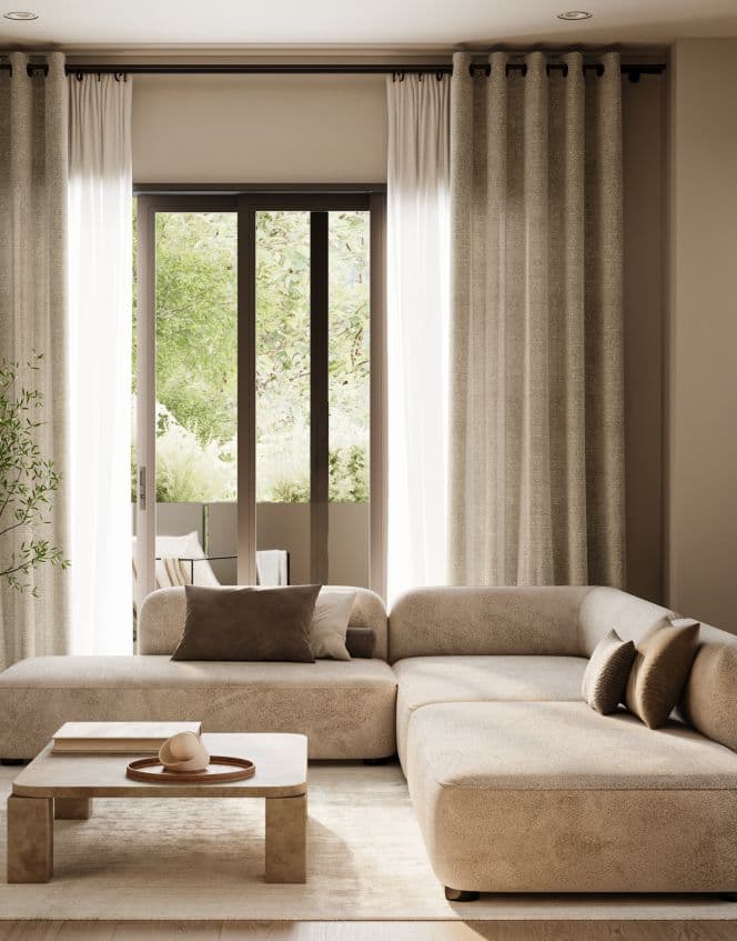 Solin – A bright living room features a low-profile, beige sectional sofa with accent pillows, paired with a low stone coffee table in warm neutral tones. Large glass sliding doors are framed by full-length linen drapes, opening out onto a private patio surrounded by lush green foliage.
